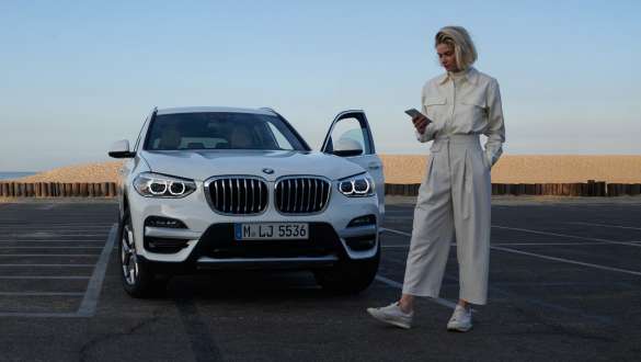 Приложение My BMW, женщина со смартфоном перед своим BMW Приложение My BMW, женщина со смартфоном перед своим BMW