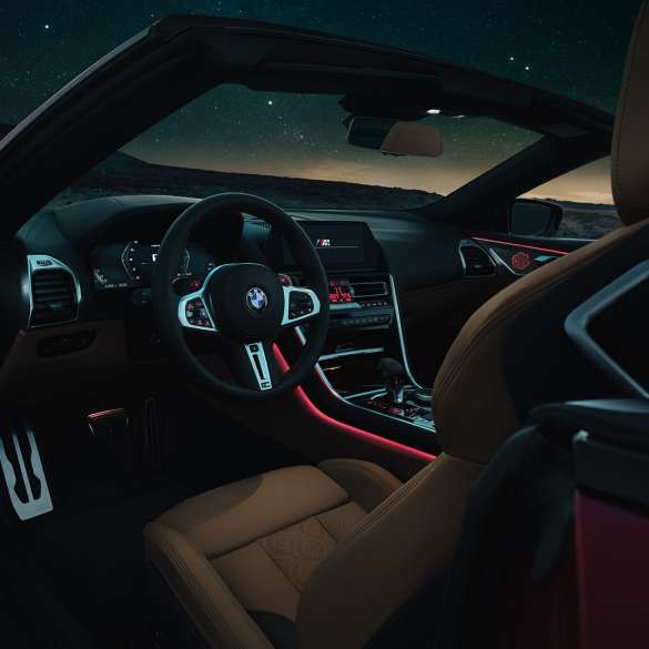 BMW M8 Competition Кабриолет, кабина. BMW M8 Competition Кабриолет, кабина ночью с кожаным рулевым колесом M и красным фоновым освещением.