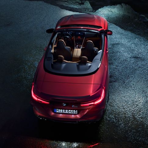 BMW M8 Competition Convertible, bird’s-eye view. BMW M8 Competition Convertible in Motegi Red metallic with open softtop, bird’s-eye view, standing at night on asphalt.