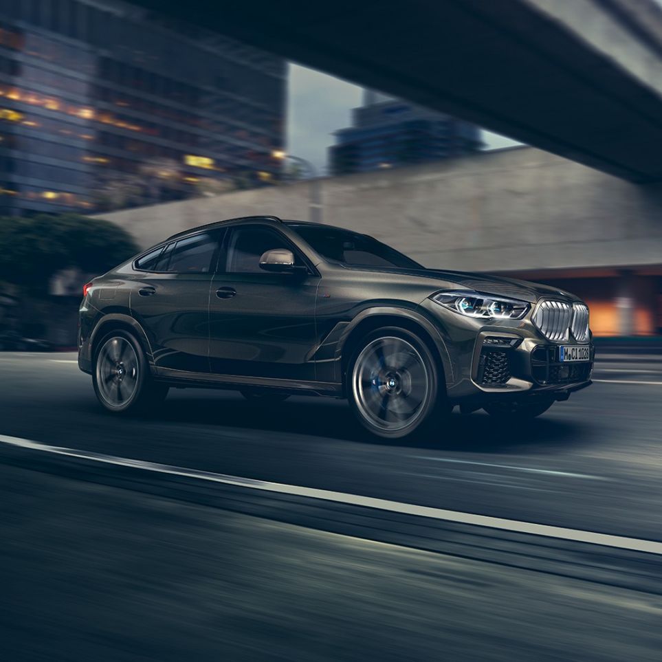 BMW X6 в движении. BMW X6, передняя часть с поворотом в три четверти в движении перед городской обстановкой.