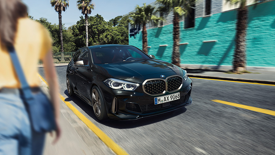 BMW 1 серии M135i xDrive, вид спереди с поворотом в три четверти. BMW 1 серии M135i xDrive, вид спереди с поворотом в три четверти с человеком на переднем плане.