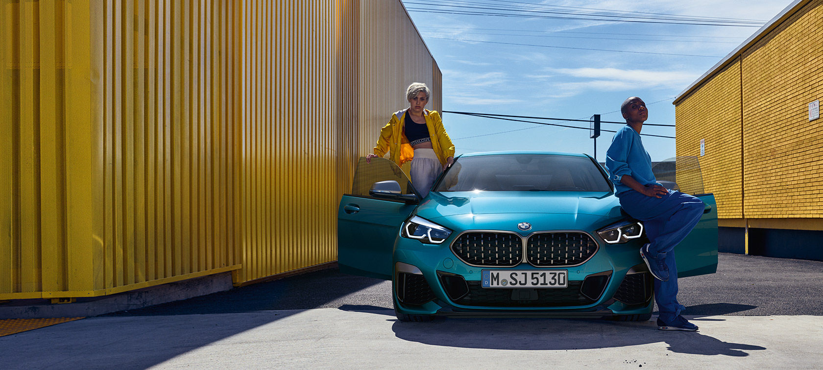 BMW 2 серии Gran Coupe F44, вид спереди BMW 2 серии Gran Coupe F44, Синий Снэппер Рокс, вид спереди с открытыми дверями и двумя людьми у автомобиля