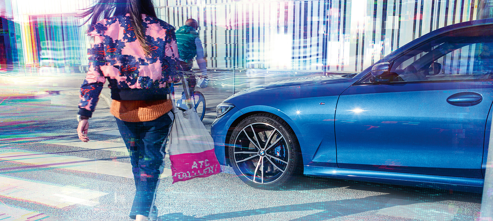 BMW 3 серии Седан, боковой снимок, три четверти. Боковой снимок седана BMW 3 серии на асфальте перед городским фоном с пассажирами с поворотом в три четверти.