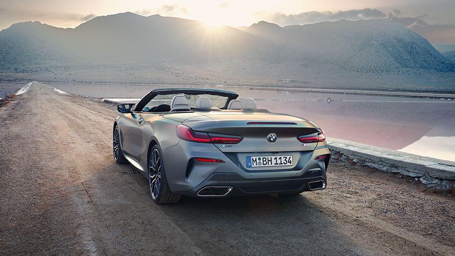BMW 8 серии Cabrio G14 LCI (рестайлинг 2022 года) эксклюзивного цвета BMW Individual Морозный Серый металлик с убранным мягким верхом в статике на фоне песчаной дороги, вид сзади