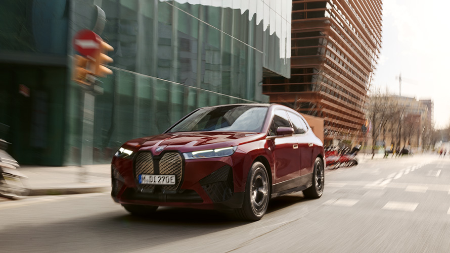 Электрический SUV BMW iX i20 xDrive50, системы помощи водителю Электрический SUV BMW iX i20 2021 xDrive50 цвета Aventurin Red едет по городским окрестностям