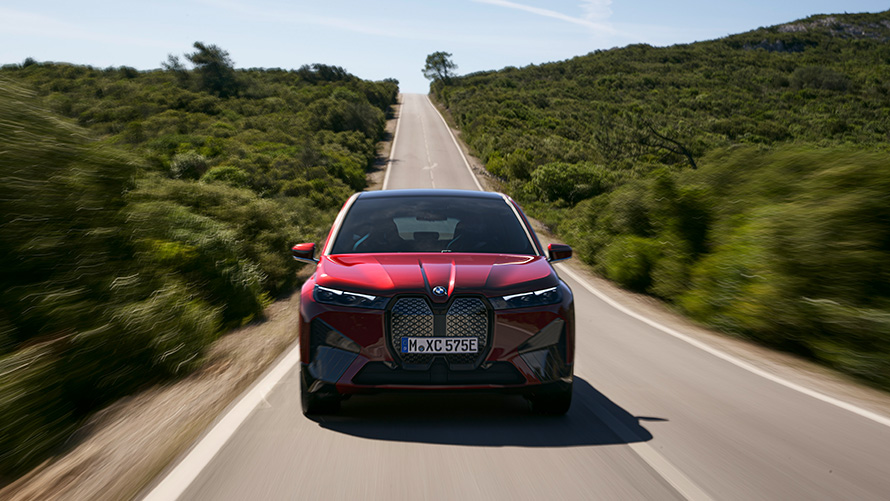 Электрический SUV BMW iX i20 xDrive50, запас хода Электрический SUV BMW iX i20 2021 xDrive50 цвета Aventurin Red едет по улице, запас хода