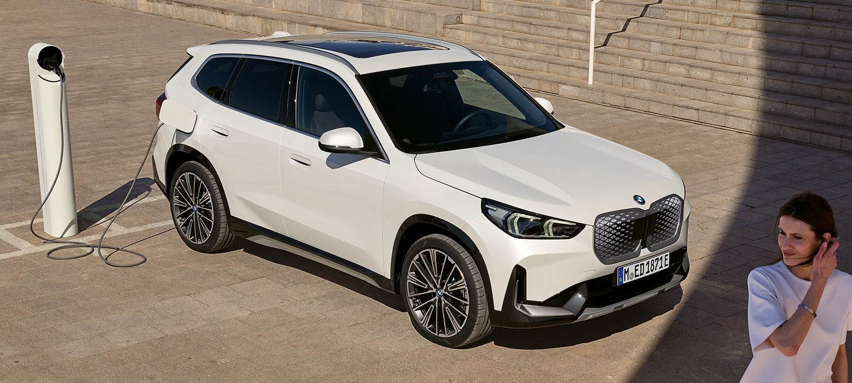 BMW iX1 U11 BEV, вид сбоку во время зарядки BMW iX1 U11 BEV 2022 в цвете Mineral White metallic, вид сбоку с поворотом в две трети во время зарядки