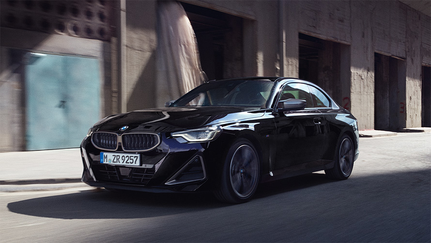 BMW M240i xDrive Coupe G42 2021 &quot;Черный Сапфир металлик&quot;, вид сбоку в три четверти в движении перед зданиями
