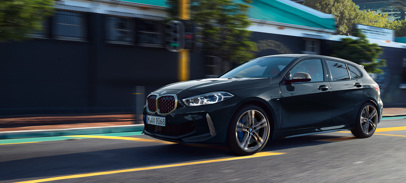 Новый BMW M135i xDrive в Black Sapphire металлик, вид сбоку за рулем с поворотом в три четверти.