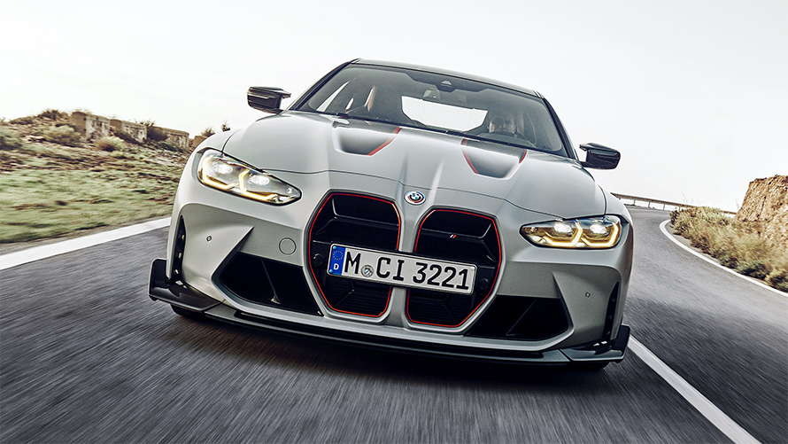 BMW M4 CSL G82 в цвете BMW Individual Frozen Brooklyn Grey металлик, радиаторная решетка черного цвета с фирменным красным покрытием, вид спереди в движении на улице.