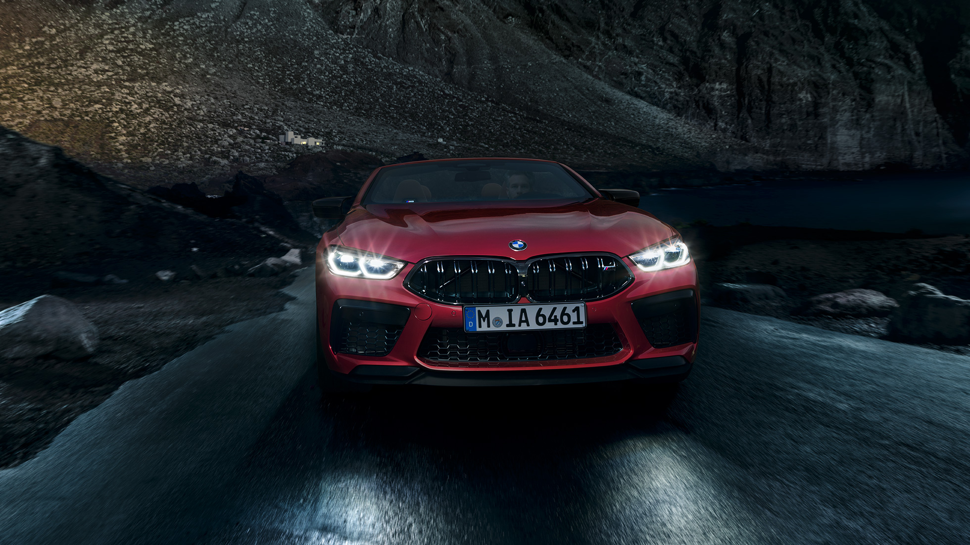 BMW M8 Competition Кабріолет, вид спереди. BMW M8 Competition Кабріолет в Motegi Red металлик с включенными фарами, вид спереди с поворотом в три четверти, вождение ночью.