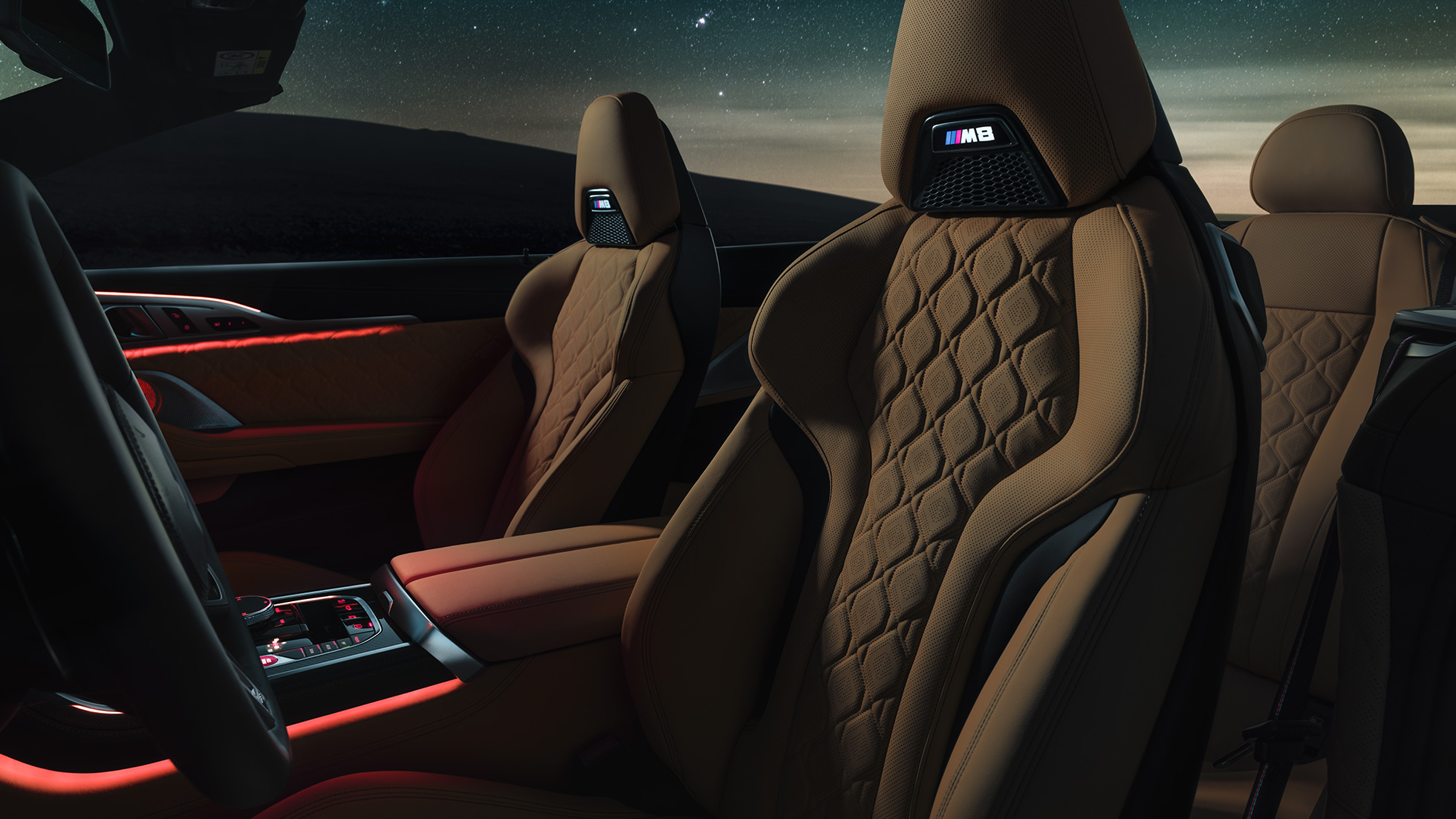 Спортивные сиденья в коже 'Merino'. BMW M8 Competition Кабриолет с открытой мягкой крышей под звездным небом, салон со спортивными сиденьями M из кожи 'Merino' и красным фоновым освещением.