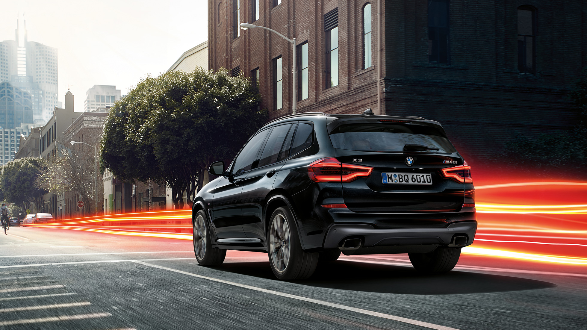 BMW X3 M40i, three-quarter rear view. BMW X3 M40i in Black Sapphire metallic, driving, exterior, three-quarter rear view before an urban background with light strips.