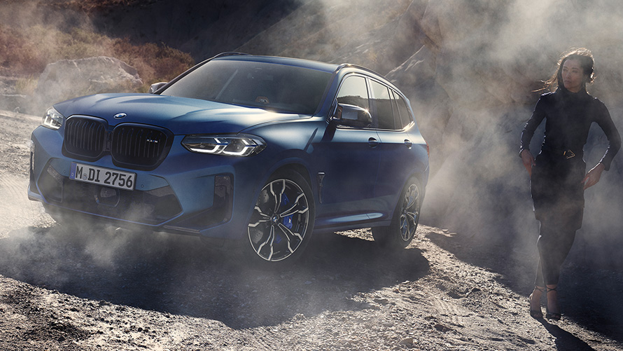 BMW X3 M Competition F97 LCI 2021, вид спереди в три четверти на каменистой местности с женщиной BMW X3 M Competition F97 LCI Facelift 2021 в цвете Frozen Marina Bay Blue металлик, вид спереди в три четверти на каменистой местности с женщиной