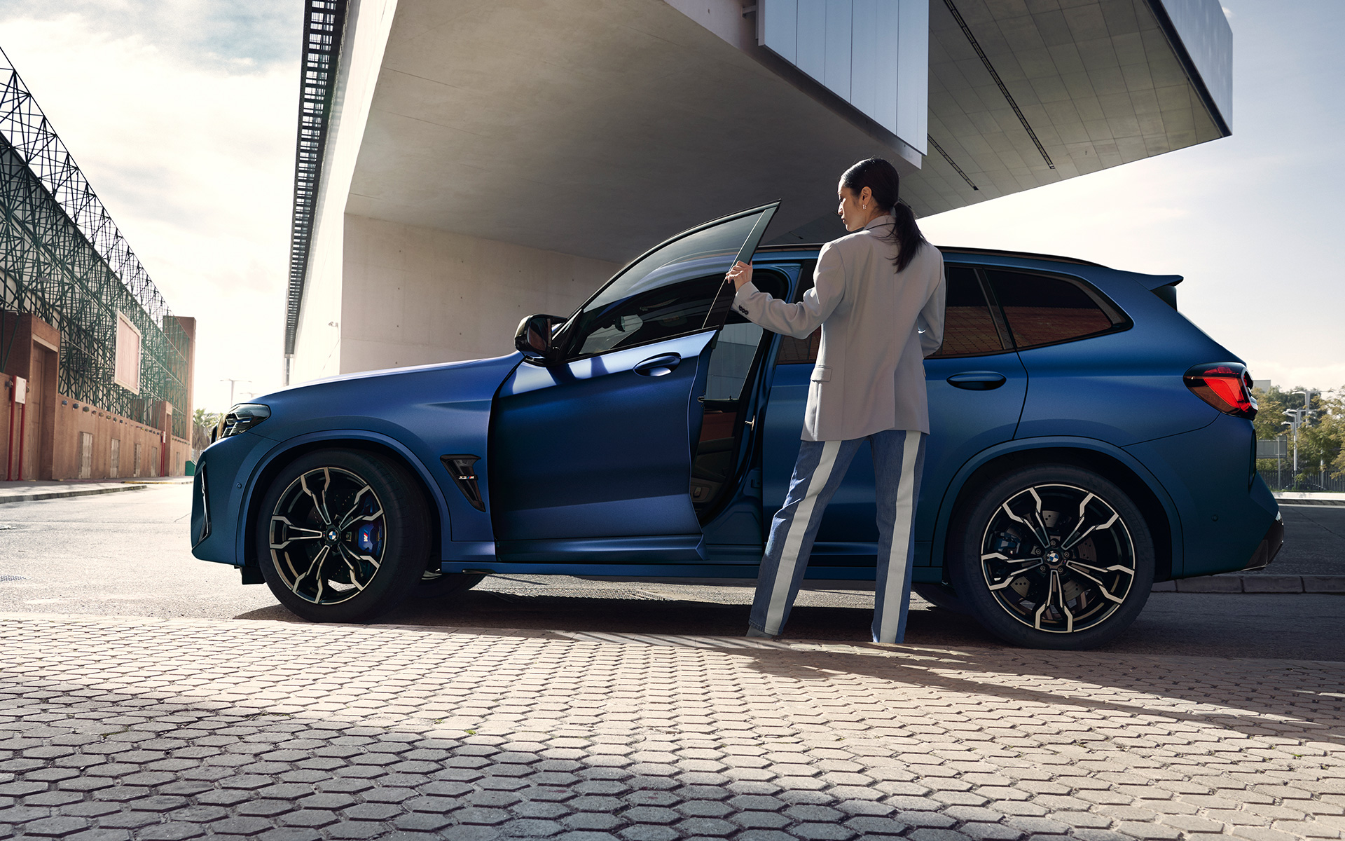 BMW X3 M Competition F97 LCI Facelift 2021 в цвете Frozen Marina Bay Blue металлик, вид сбоку с открытой дверью и женской моделью