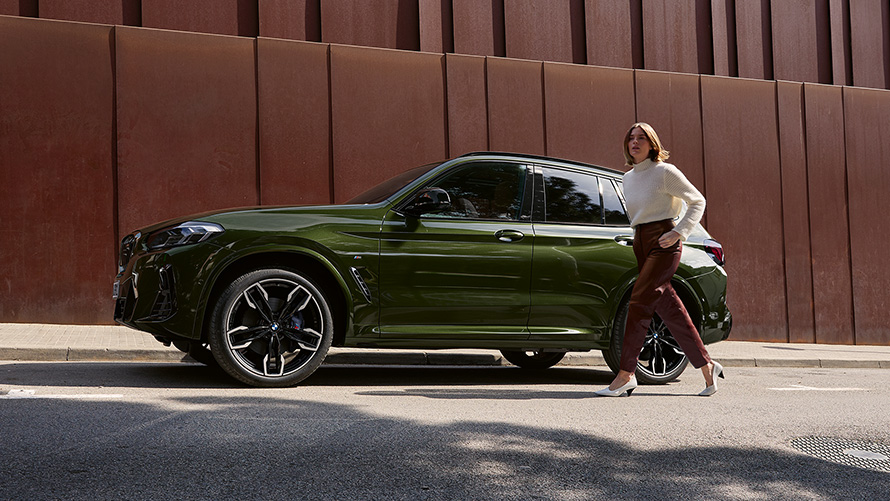 BMW X3 M G01 LCI Facelift 2021 в цвете Malachite Green металлик, вид сбоку с моделью-женщиной