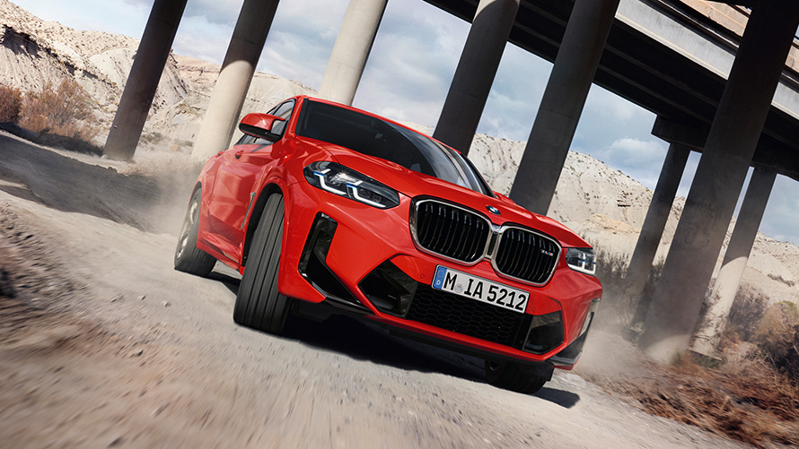 BMW X4 M F98 LCI Facelift 2021 в цвете Toronto Red металлик, вид спереди в три четверти перед колоннами моста