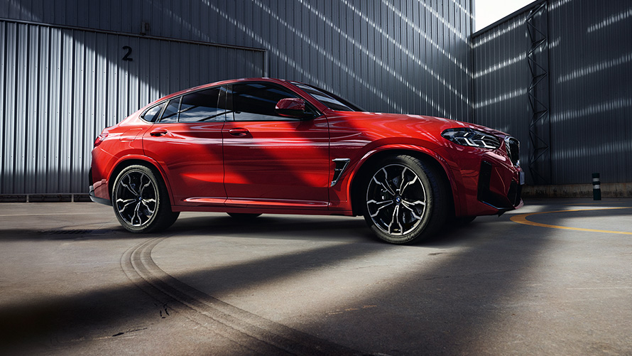 BMW X4 M F98 LCI Facelift 2021 в цвете Toronto Red металлик, вид сбоку в три четверти перед фабрикой