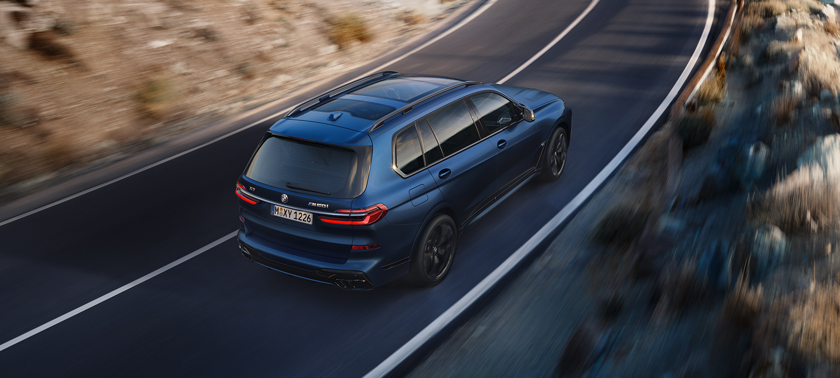 BMW X7 M60i G07 LCI синего цвета Frozen Marina Bay Blue в движении, вид сзади сверху с поворотом в три четверти BMW X7 M60i G07 LCI синего цвета Frozen Marina Bay Blue на улице, вид сзади сверху с поворотом в три четверти