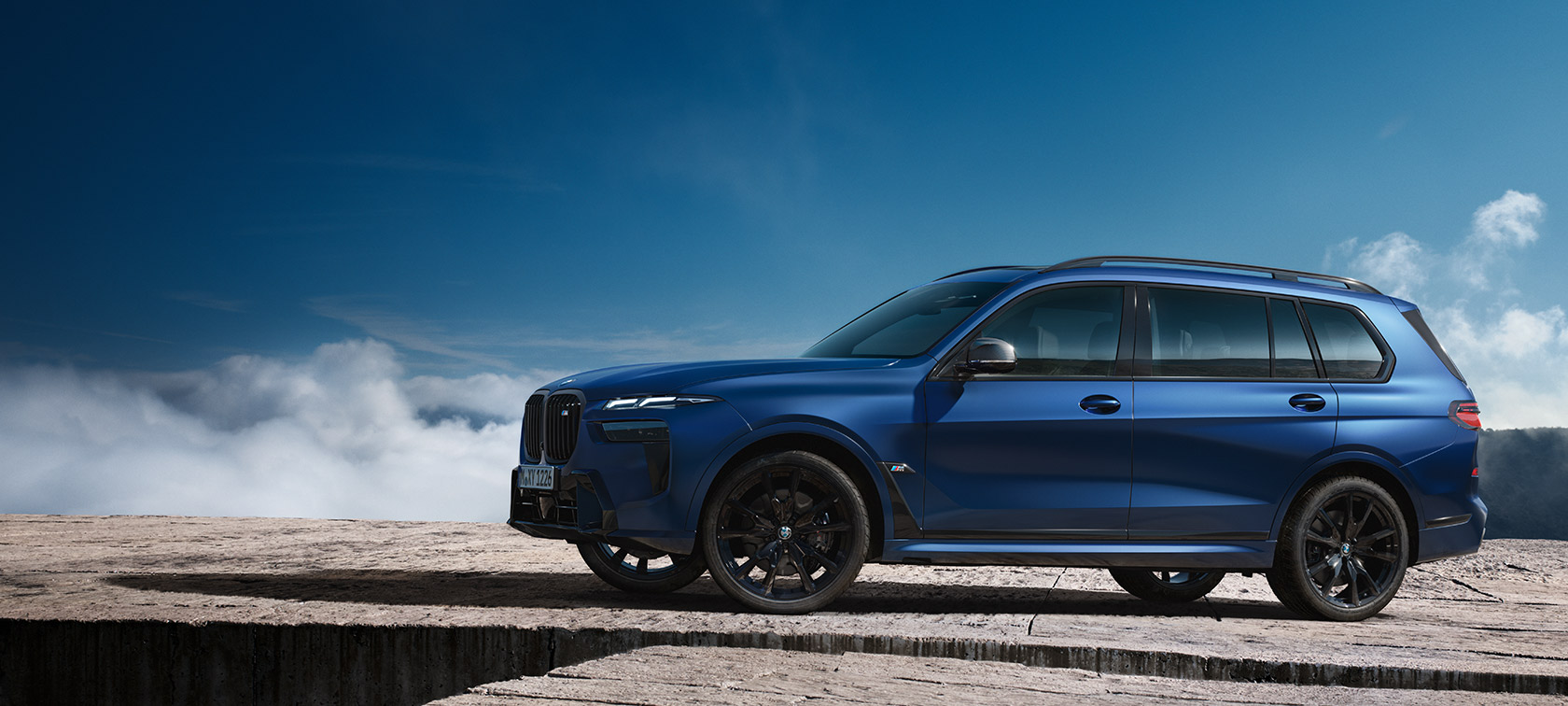 BWM X7 M60i xDrive G07 LCII окраска кузова морозный синий (Frozen Marina Bay Blue), вид сбоку, перед горным ландшафтом