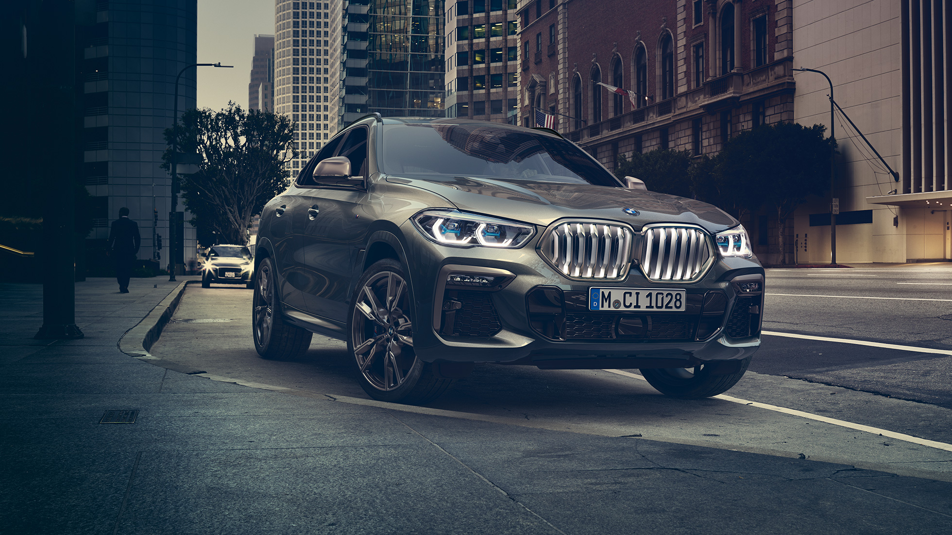 BMW X6 Adaptive M suspension Professional BMW X6 in three-quarter front perspective in front of an urban setting.