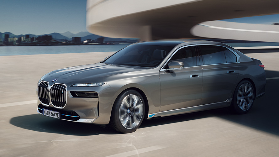 BMW M760e xDrive в сером цвете BMW Individual Dravite Grey metallic, вид спереди с поворотом в три четверти, в движении по улице