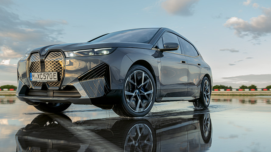 Колеса BMW, BMW iX (i20) вид спереди с поворотом в три четверти на мокрой дороге Колеса BMW, BMW iX (i20) вид спереди с поворотом в три четверти на мокрой дороге
